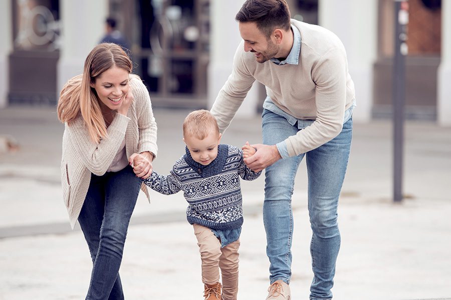 About Our Agency - Young Father and Mother Helping Their Baby to Walk in the City Street